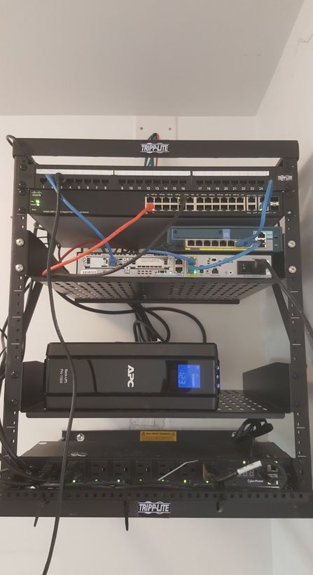 An open-frame wall rack with patch panel, switch, router and a rack-mount UPS neatly mounted